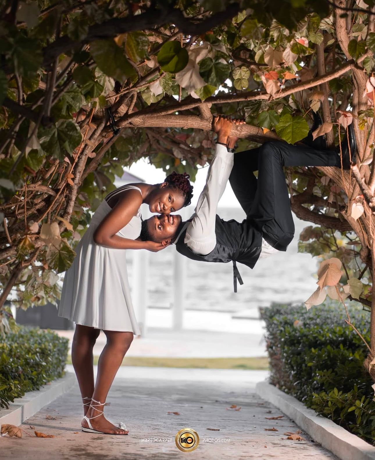 Playful couple poses under garden archway with hanging vines.