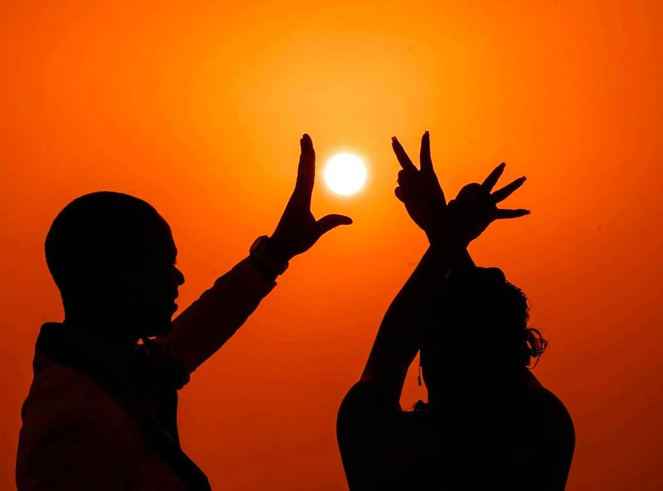 Silhouettes playfully pose against vibrant orange sunset sky.