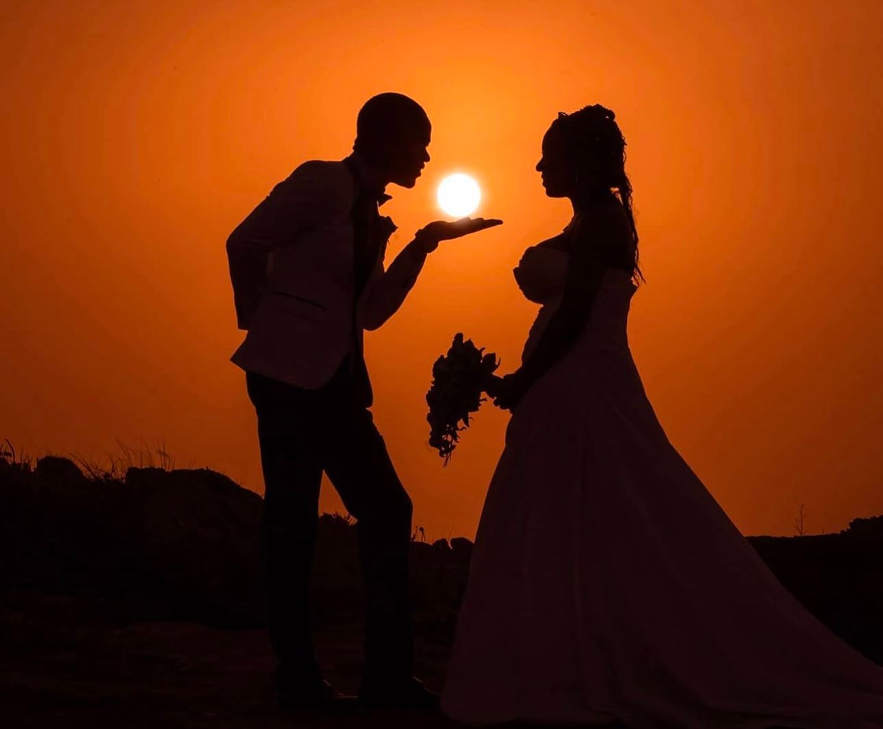 Silhouetted couple creates magical sunset photo with sun appearing to float between them.
