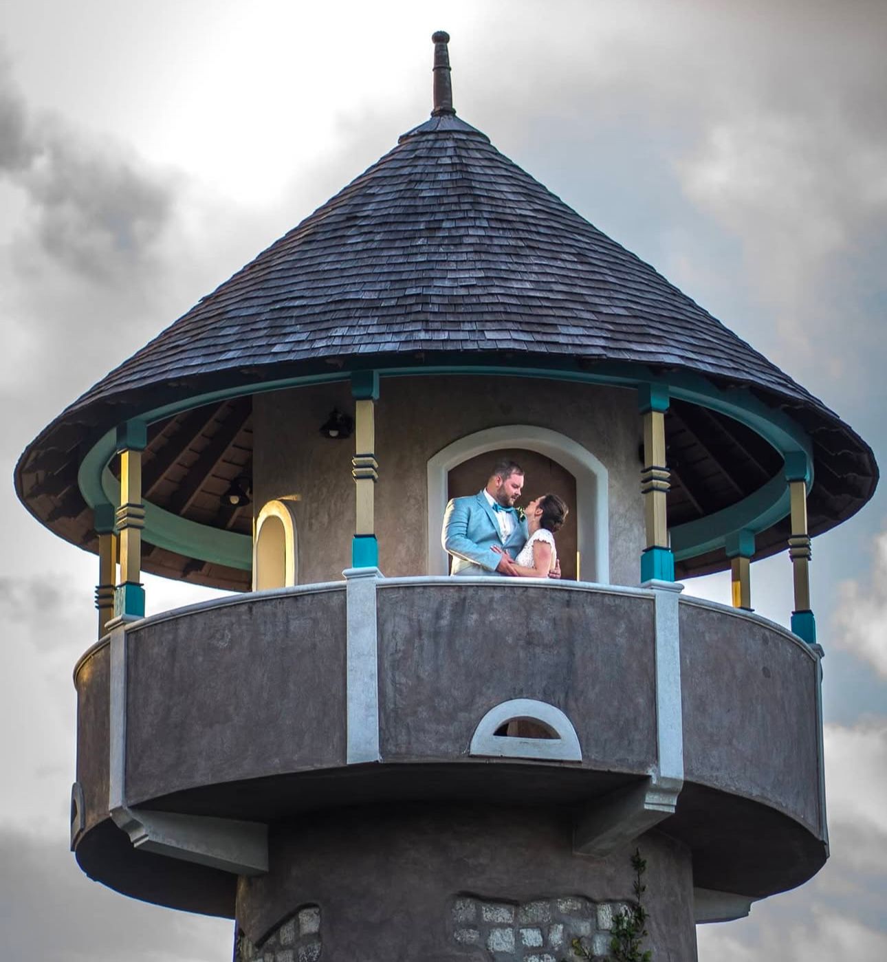 Wedding rings displayed on a decorative gazebo tower with cloudy sky in the background.