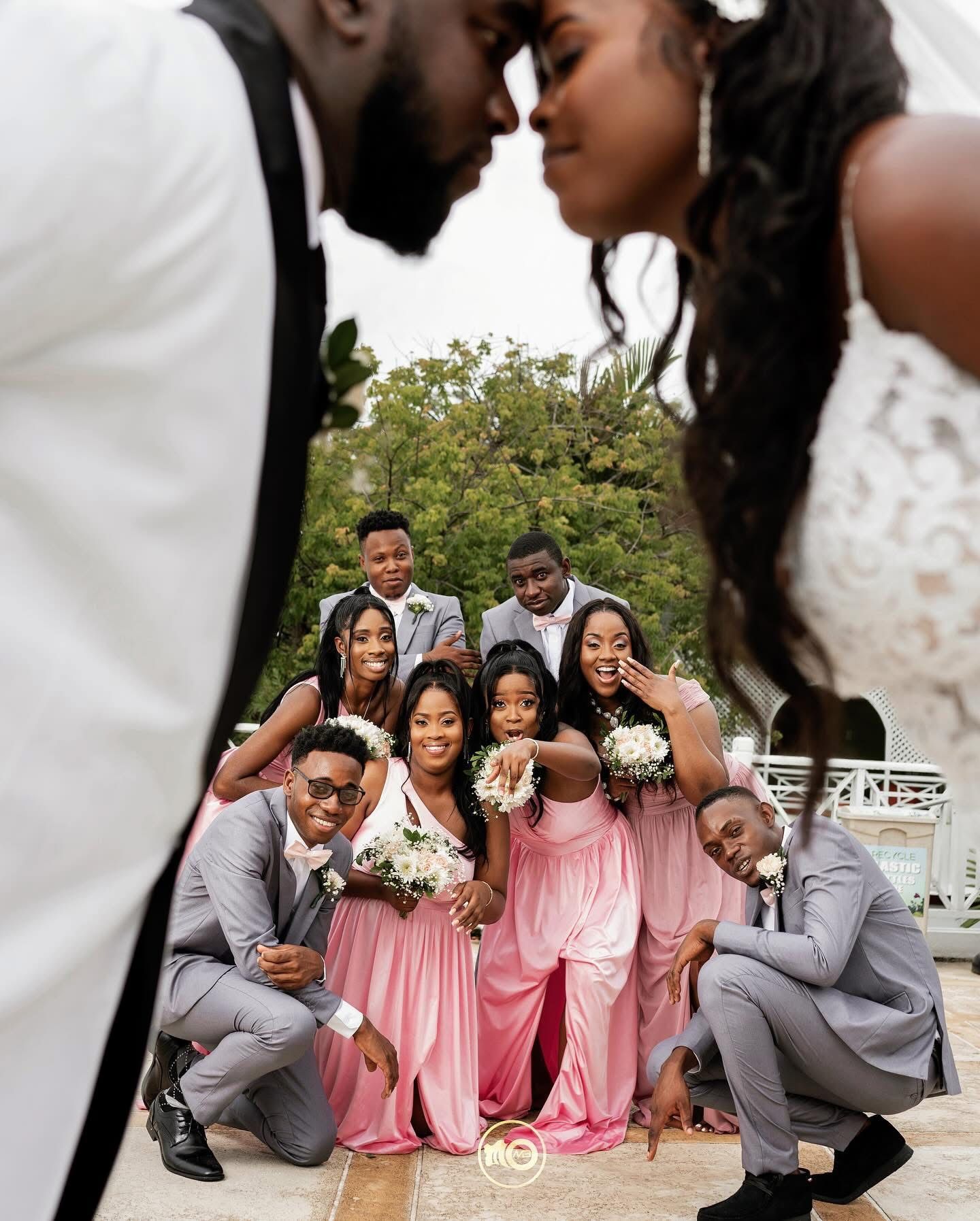 Wedding party in pink and gray attire posing playfully for group photos.