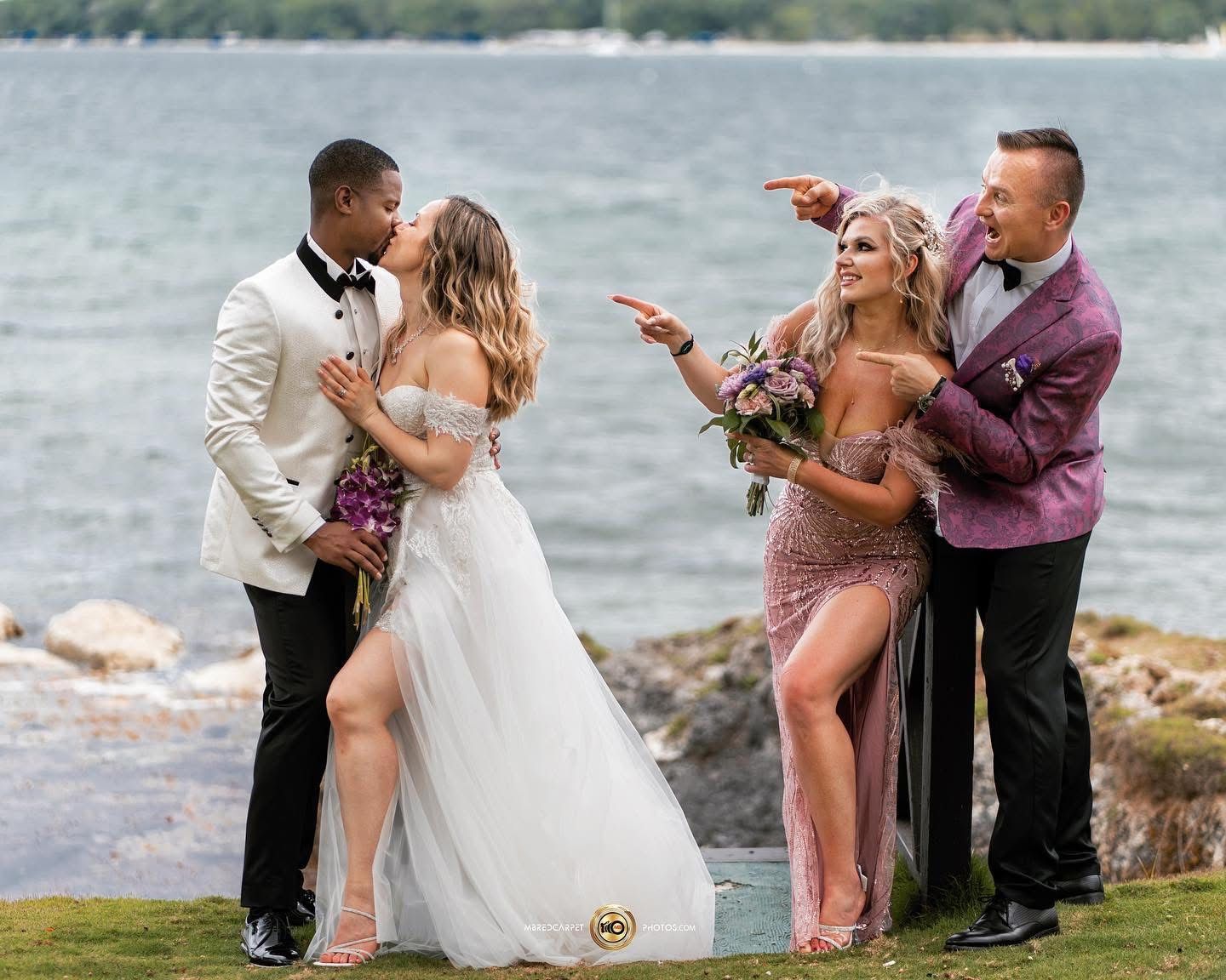 Wedding party celebrates with playful poses and dance moves along a scenic waterfront setting during sunset.