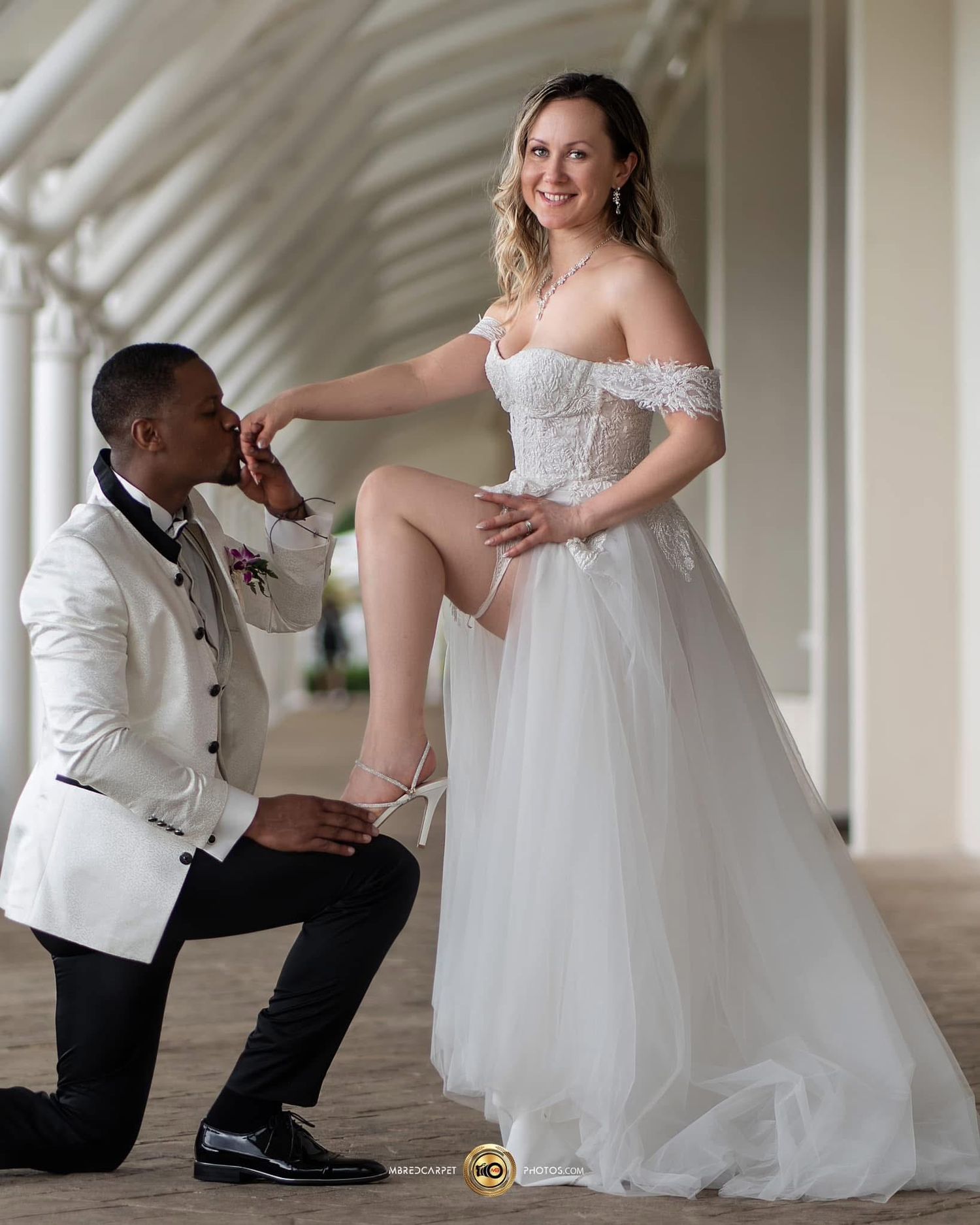 A couple shares a playful moment during their wedding photoshoot in a bright hallway with white columns.