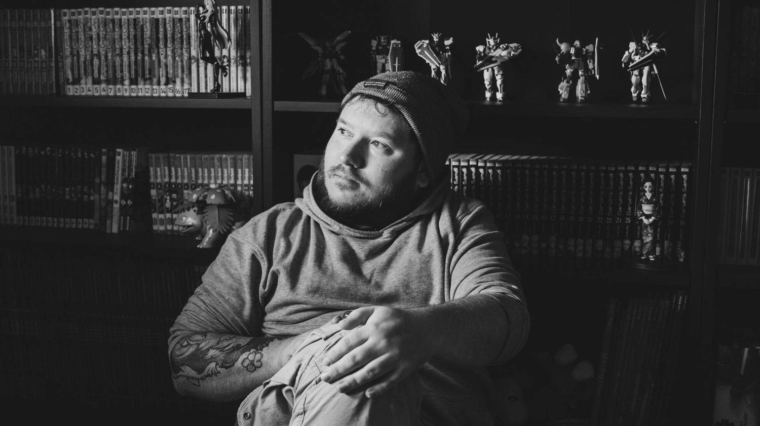 Black and white portrait of person in casual sweater sitting in front of bookshelves in contemplative pose.
