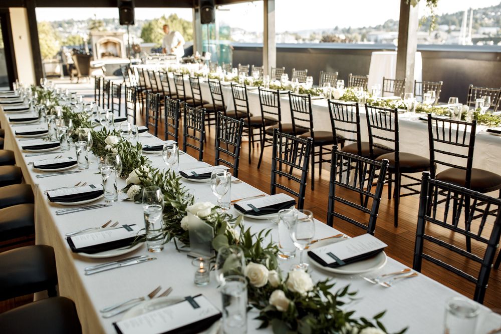 A formal wedding reception setup with long tables, chiavari chairs and greenery runners.