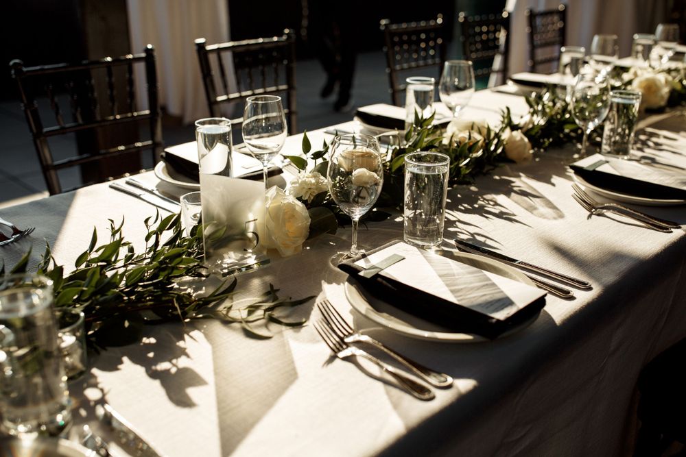 An elegant wedding reception table with white florals and greenery garland centerpieces.