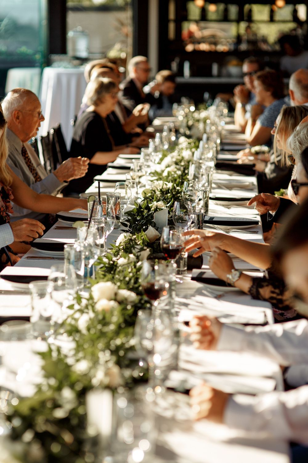 Wedding guests enjoy a meal at an elegantly decorated long table with floral centerpieces.