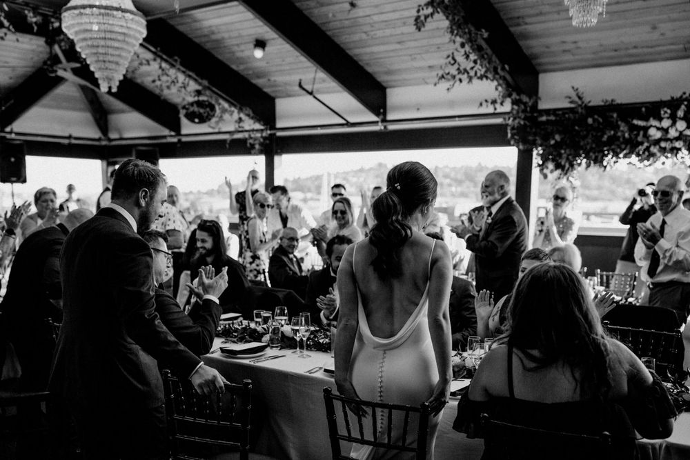 Black and white wedding reception photo showing backlit couple and guests in indoor venue.