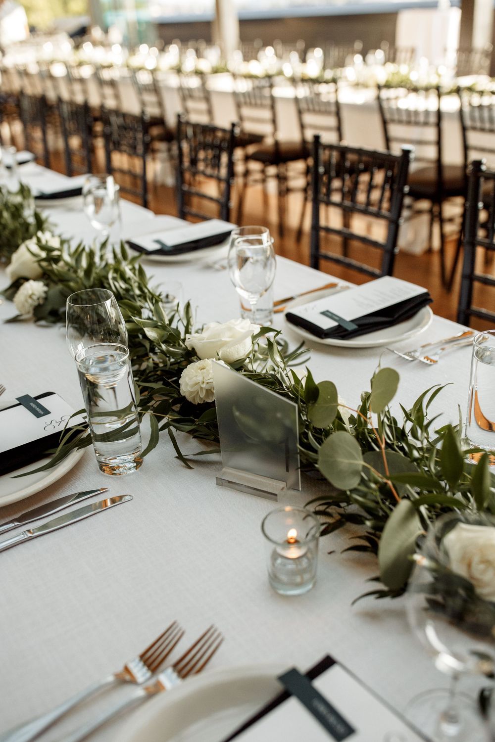 Long reception tables set with white linens, greenery runners and classic place settings.