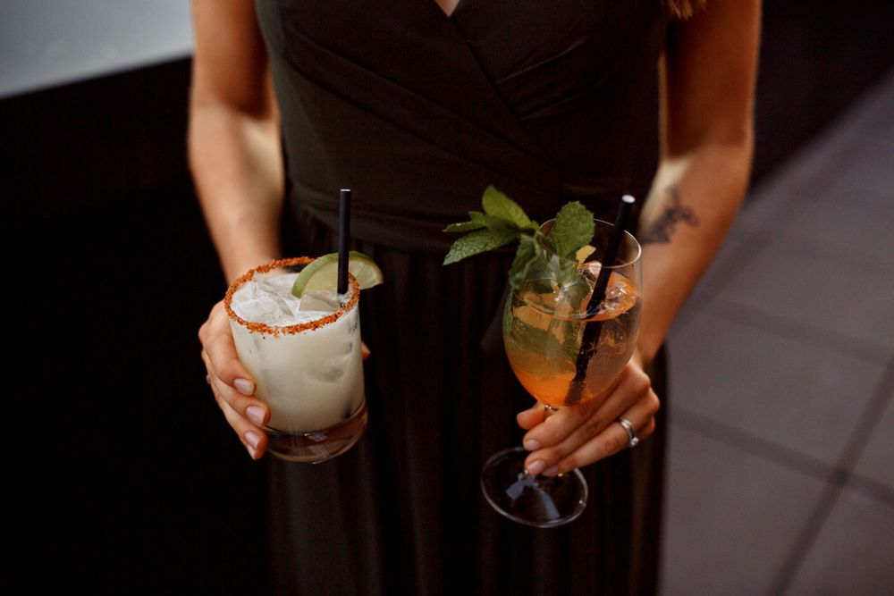 Elegant cocktails being held by server in black dress against dark background.