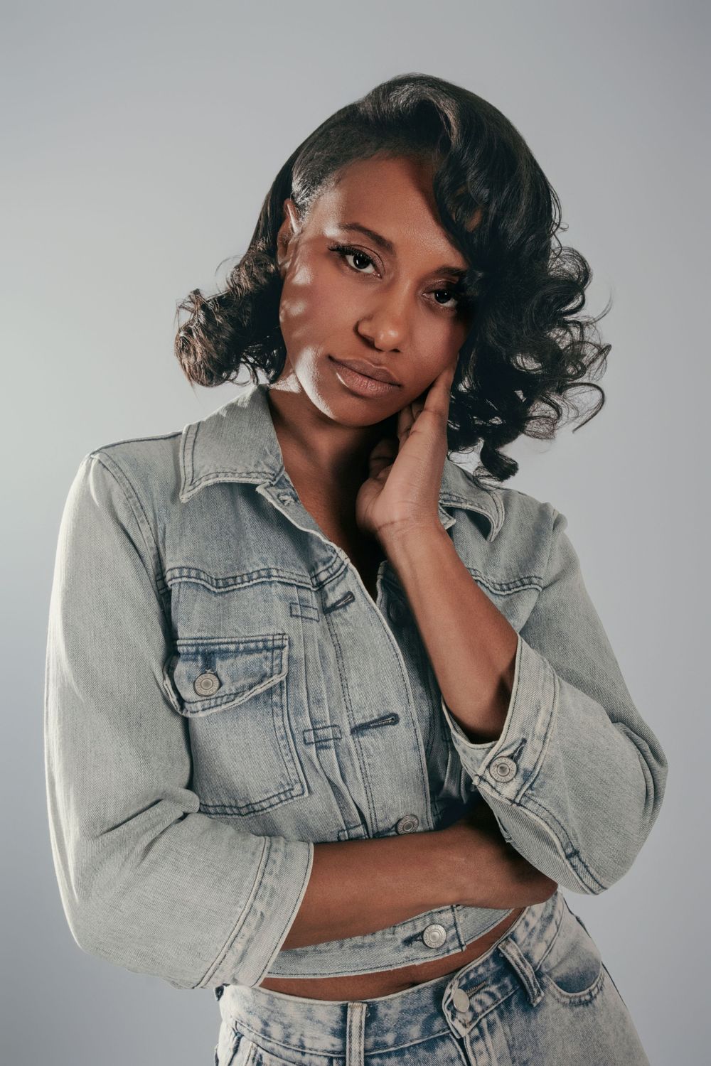 Model in cropped denim jacket strikes series of casual poses against gray studio background.