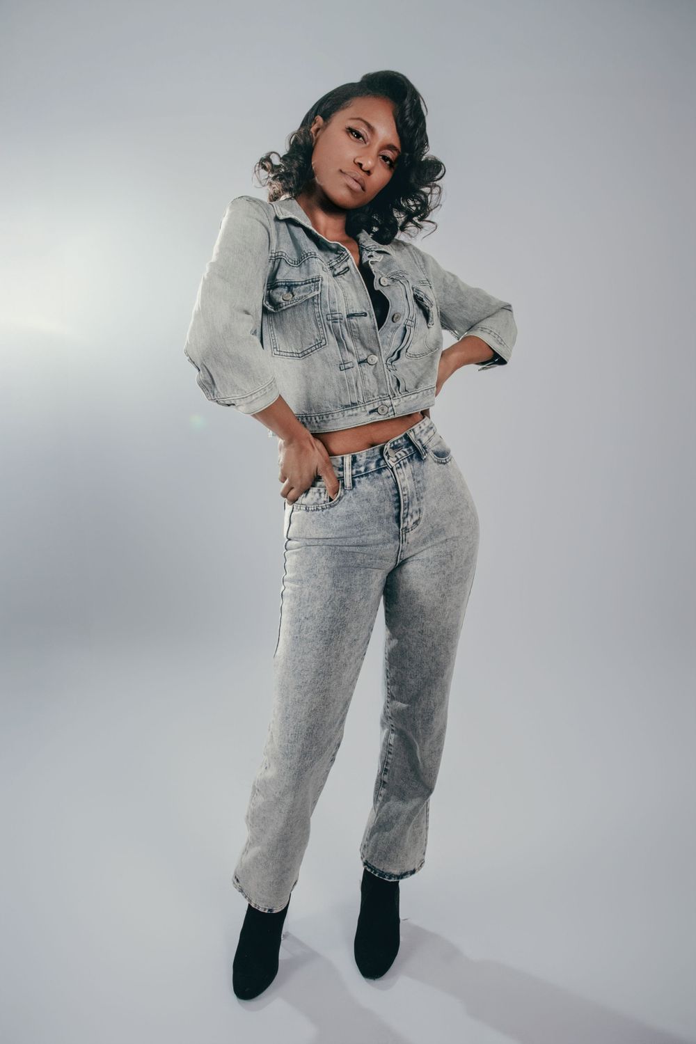 Model wearing light wash denim ensemble poses dynamically in studio setting.