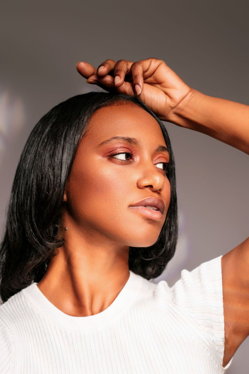 Fashion model in white top poses elegantly against neutral backdrop with dramatic lighting and shadows.