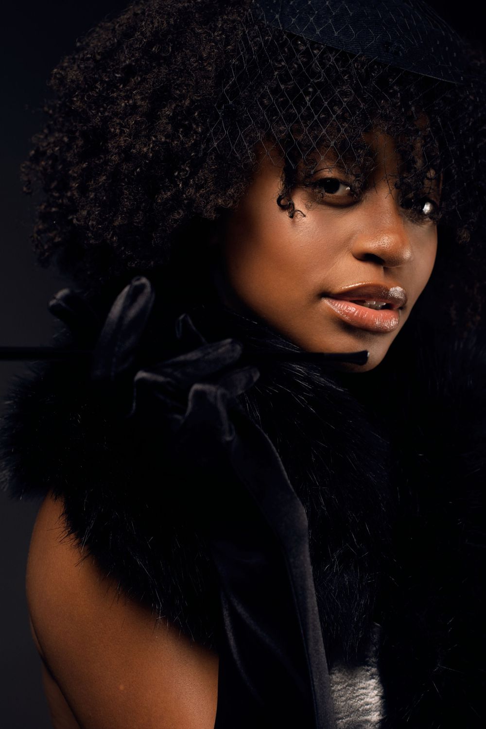 Dramatic low-key portrait with natural curly hair against dark background.