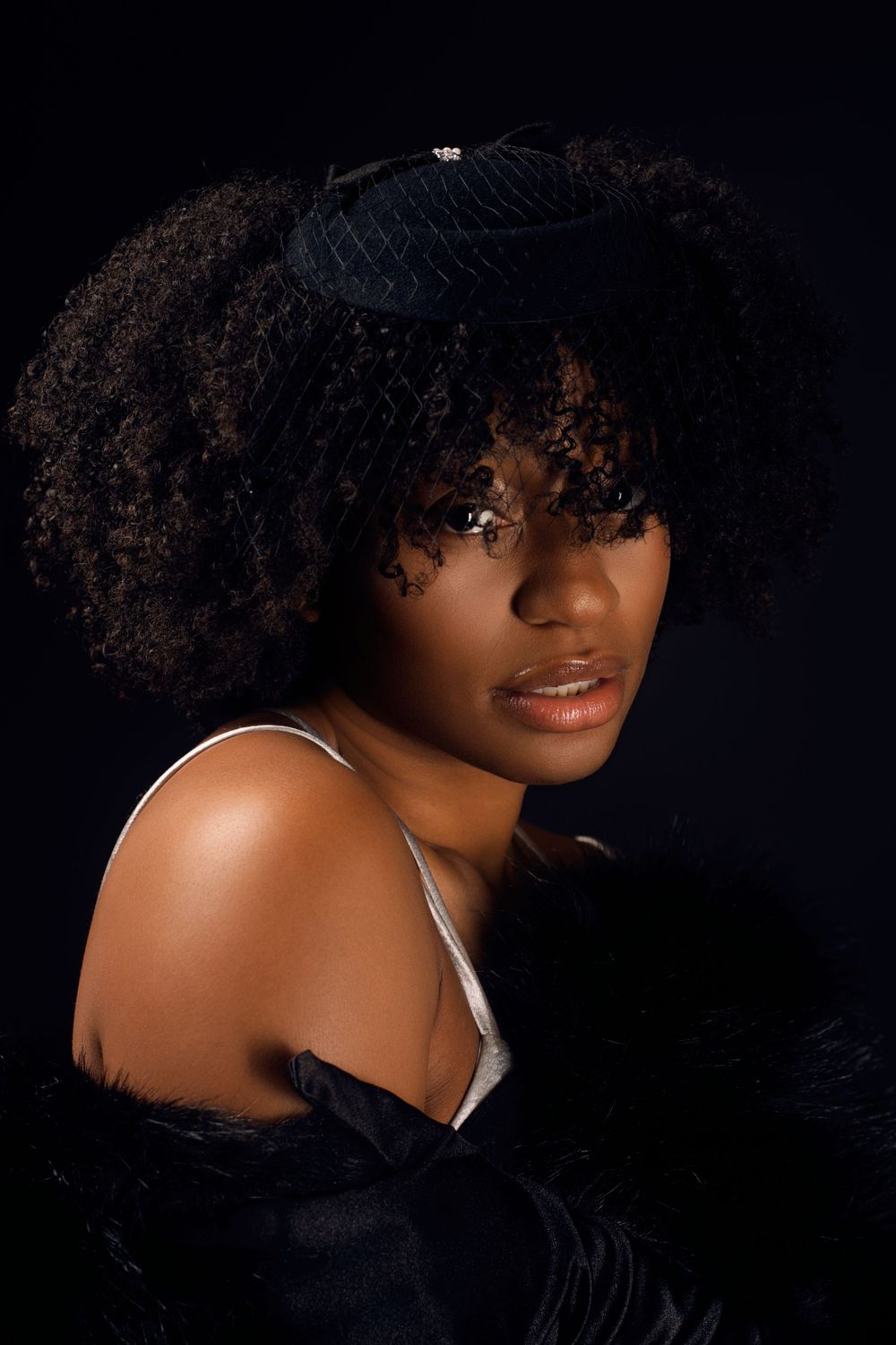 Studio portrait with natural curly hair and white top against dark background.