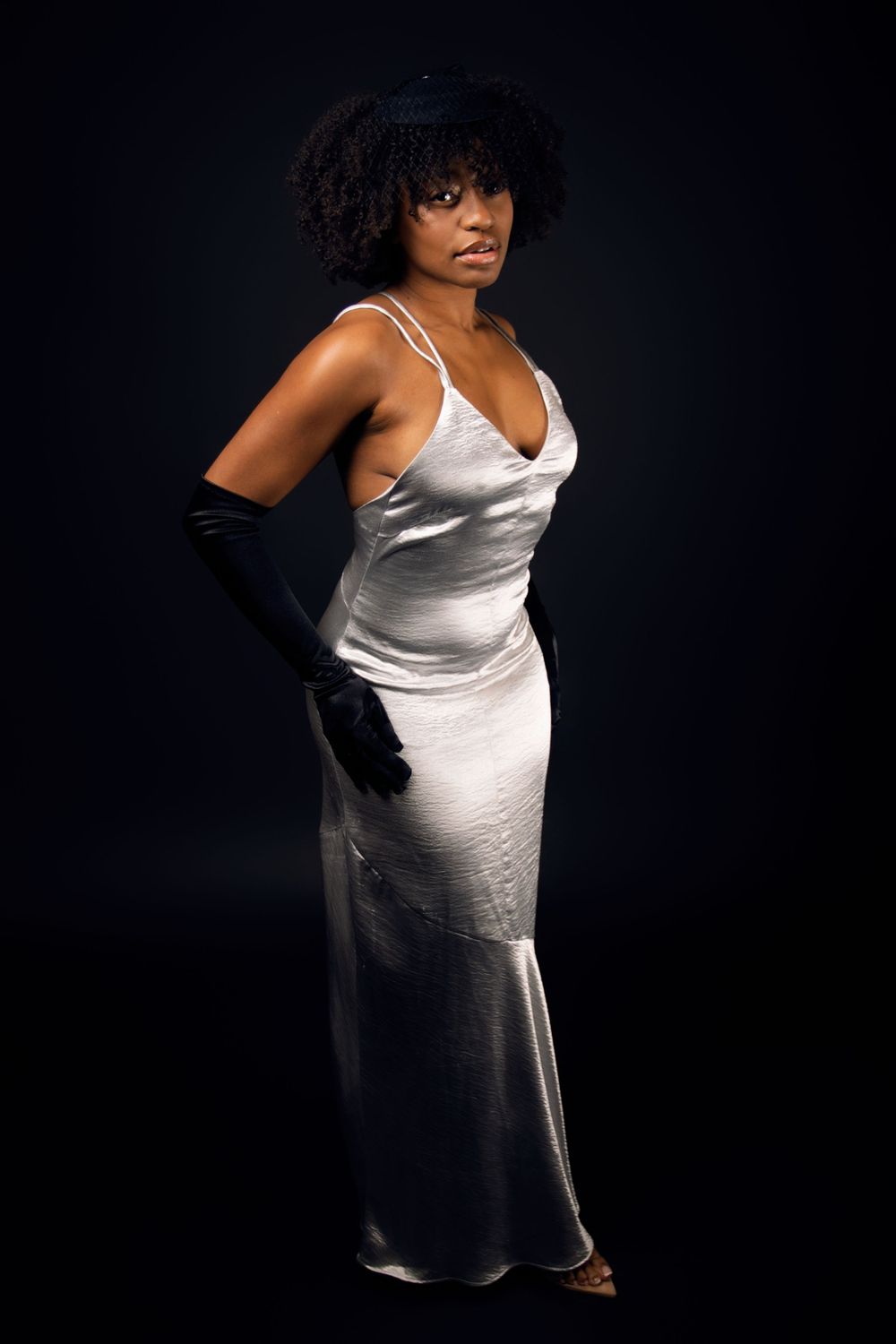 Model in white satin slip dress poses against dark studio background.