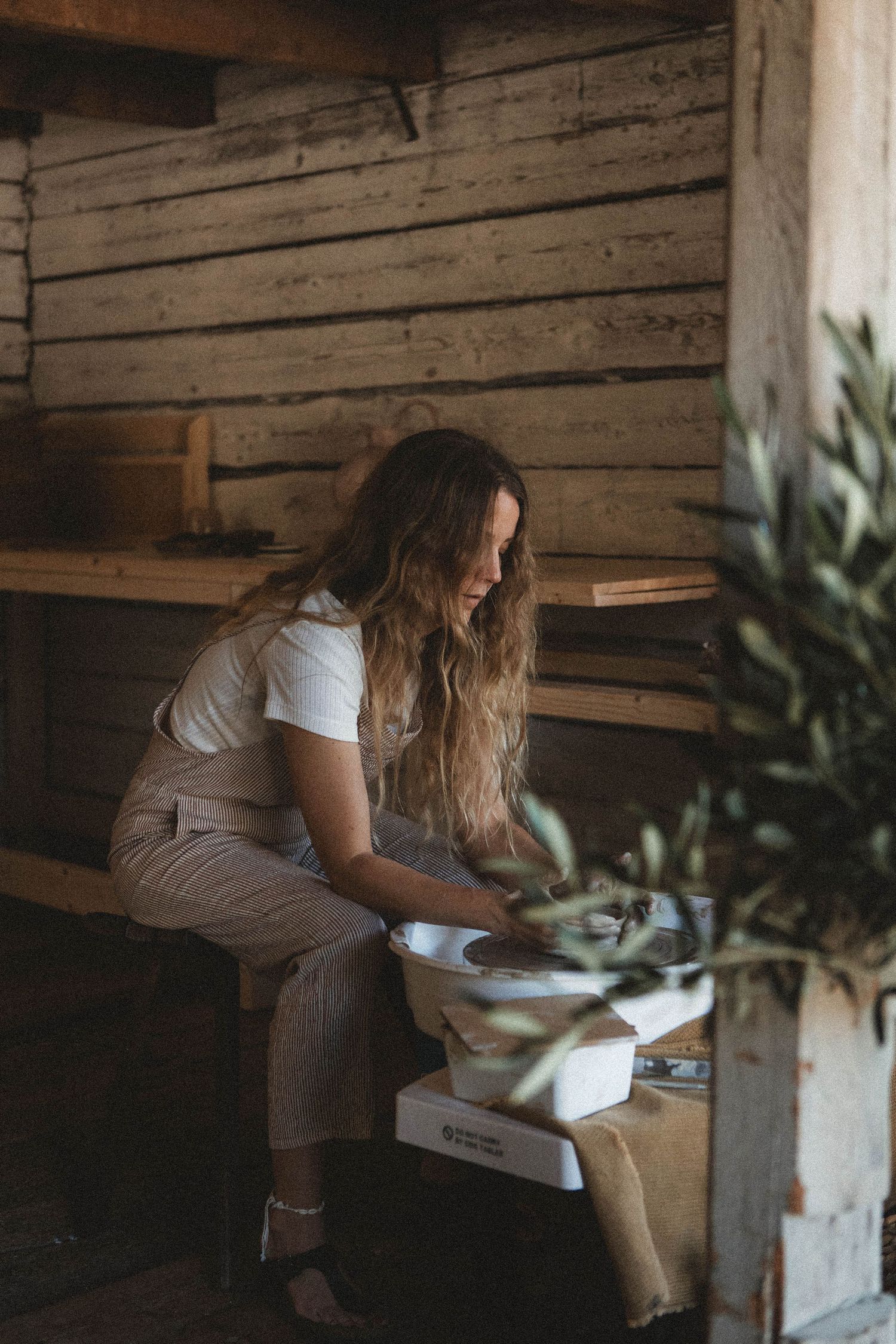 Artist working on pottery in rustic wooden studio with natural lighting.