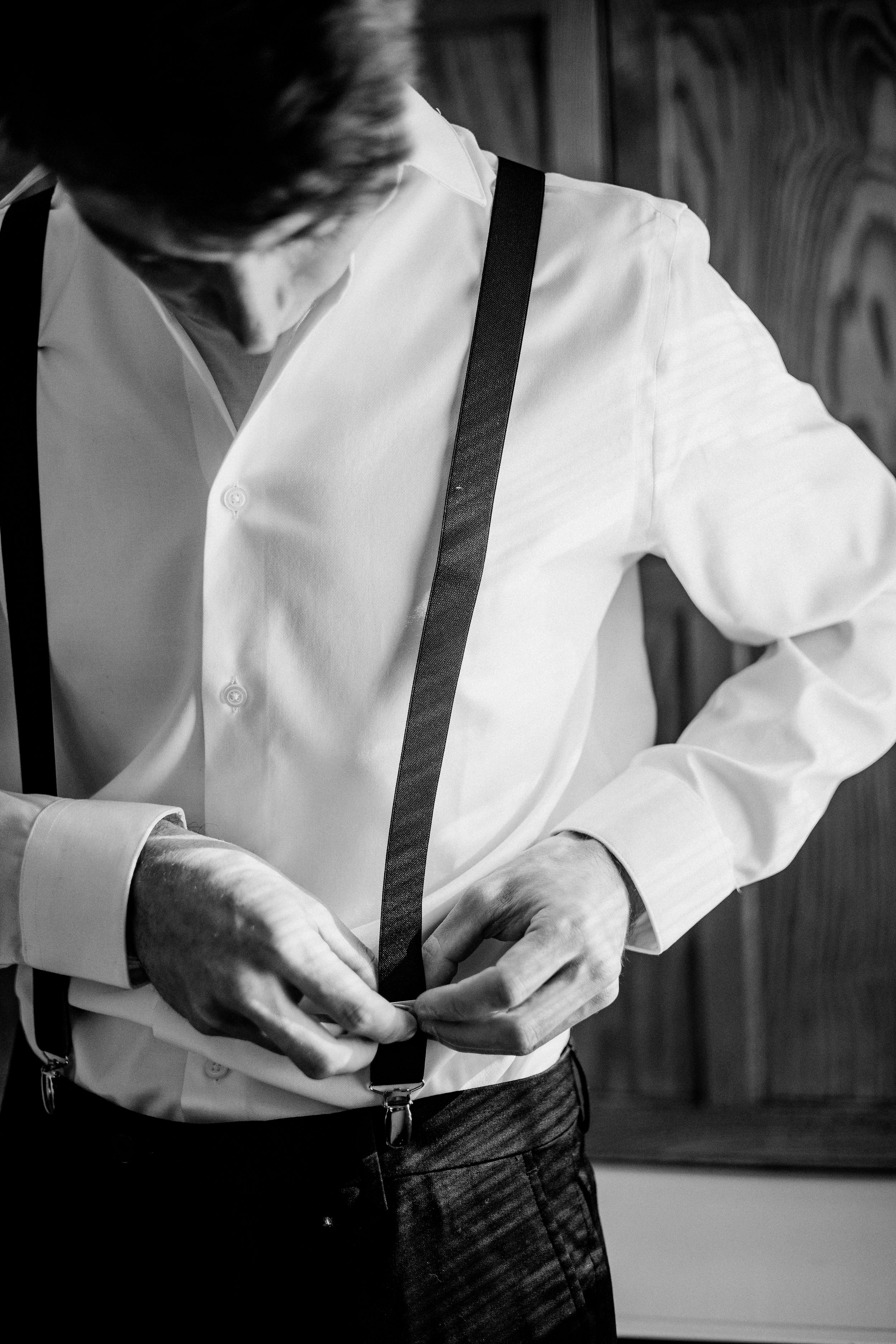 Black and white photo of a person adjusting suspenders while getting dressed.