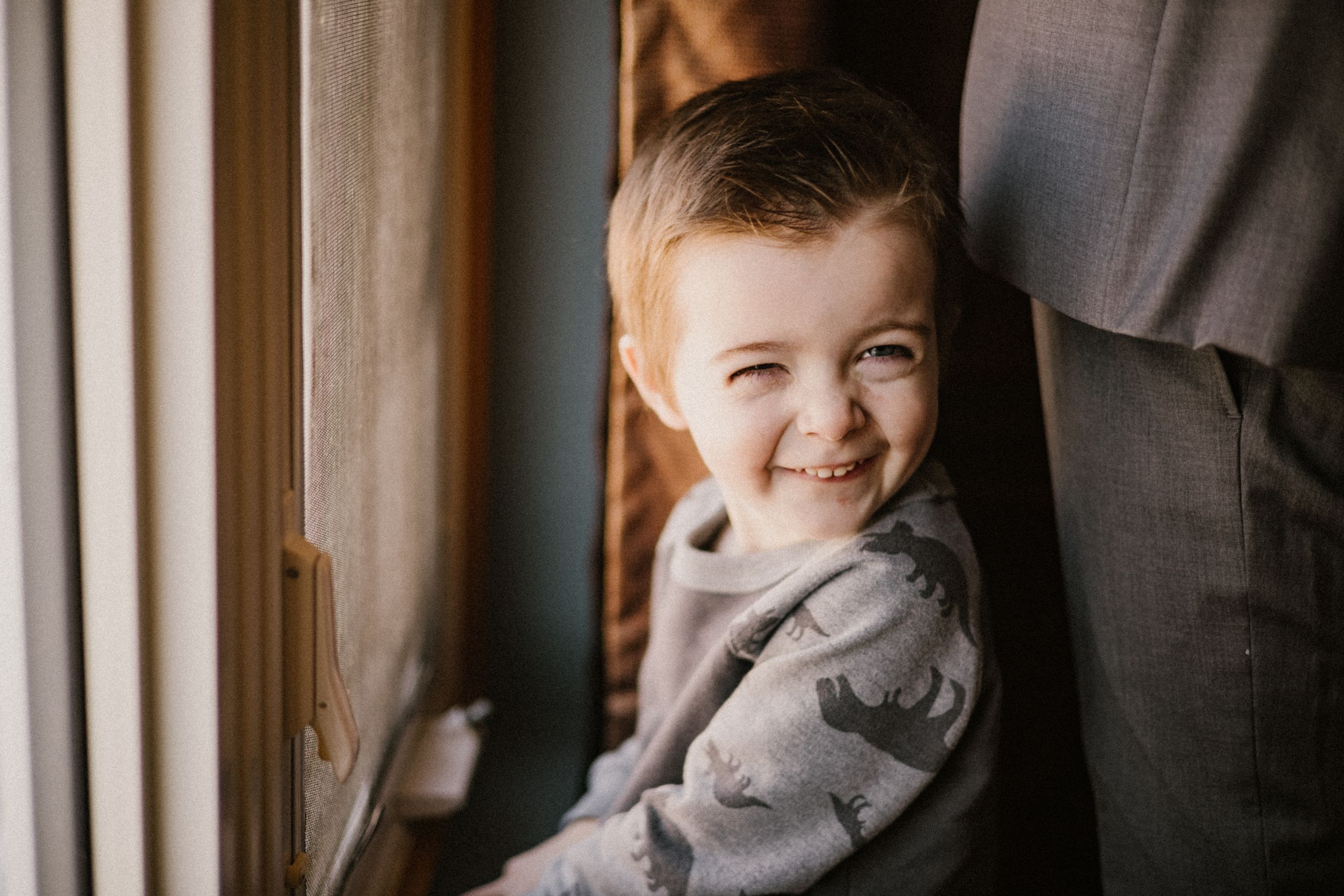Young child smiling sweetly while leaning against a window frame.