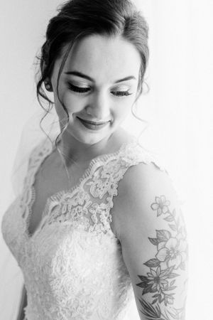 Close up portrait of bride in lace dress with floral arm tattoo.