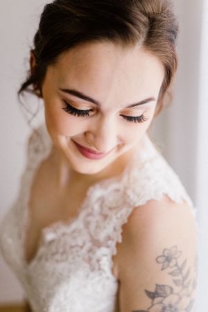 Close up portrait of bride with subtle smile showing lace dress detail and floral tattoo.