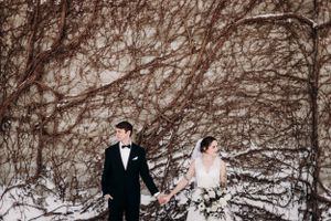 Winter wedding couple standing together against a snow-covered vine wall.
