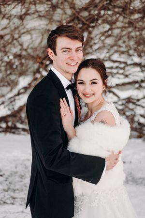 Winter wedding portrait with couple embracing in front of snow-covered branches.