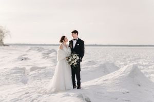 Wedding couple standing on snowy lakefront with white winter landscape.