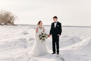 Elegant winter wedding portrait on a snow-covered beach with lake view.