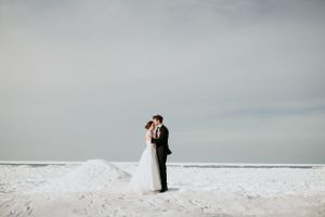 Dramatic winter wedding photo of couple embracing on snowy beach.