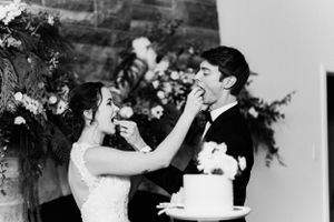 Black and white photo of newlyweds playfully feeding each other wedding cake.