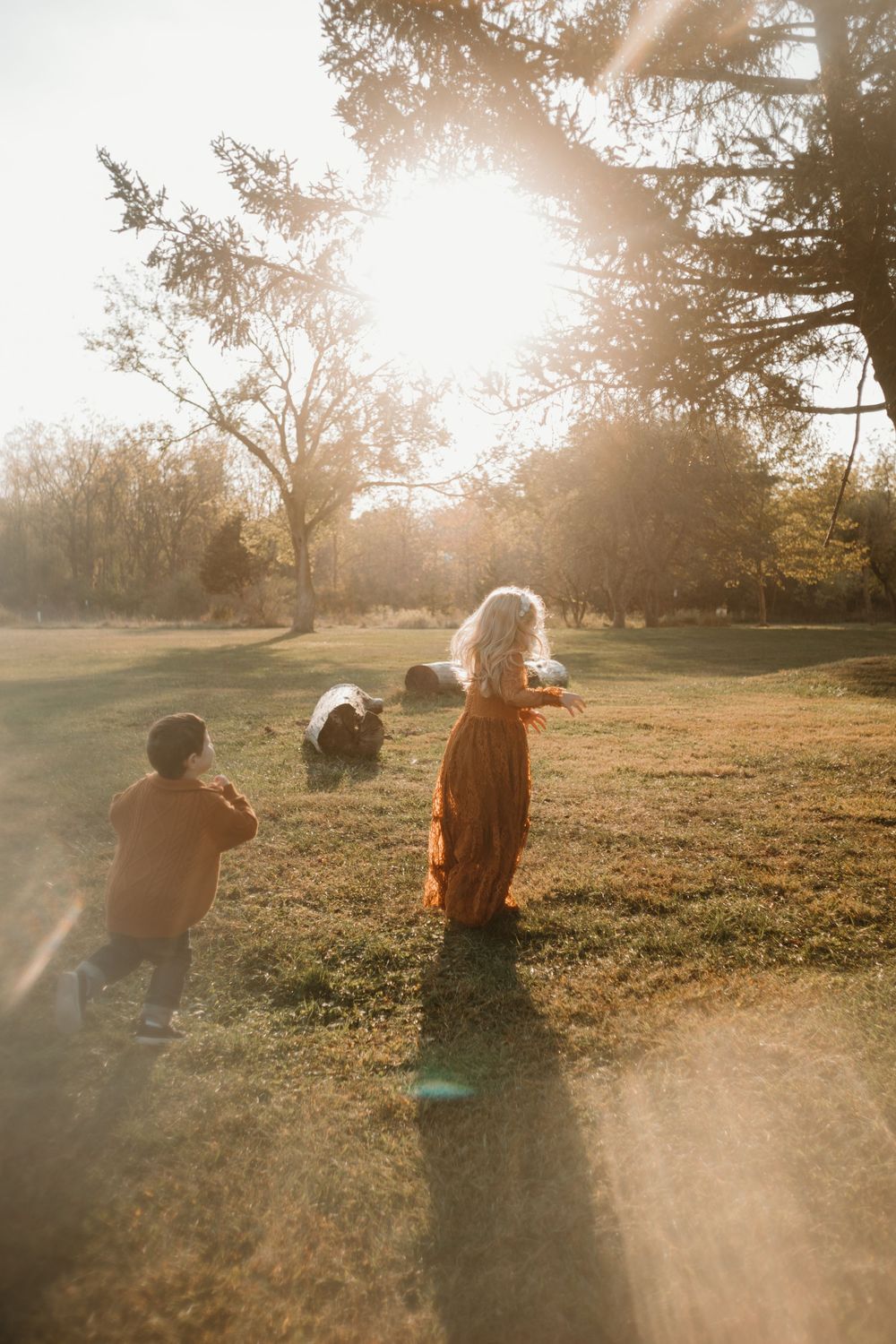 Two people sit together in a grassy field at sunset as golden sunlight streams through the trees creating a dreamy atmosphere.