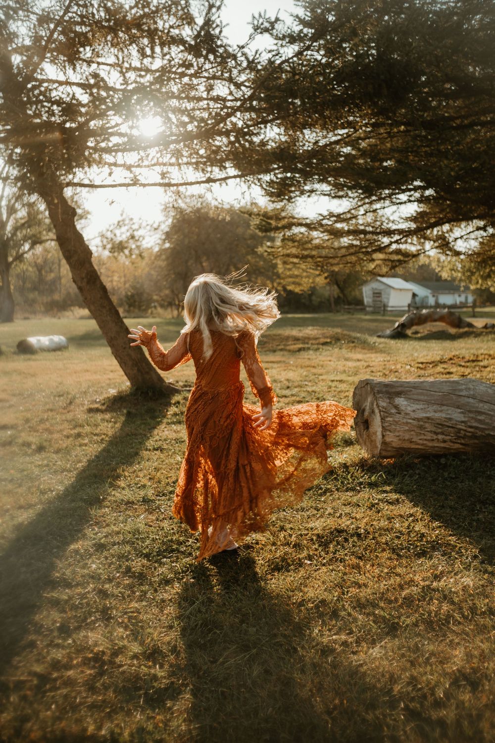 A flowing rust-colored dress twirls gracefully in golden sunlight against a pastoral landscape at sunset.