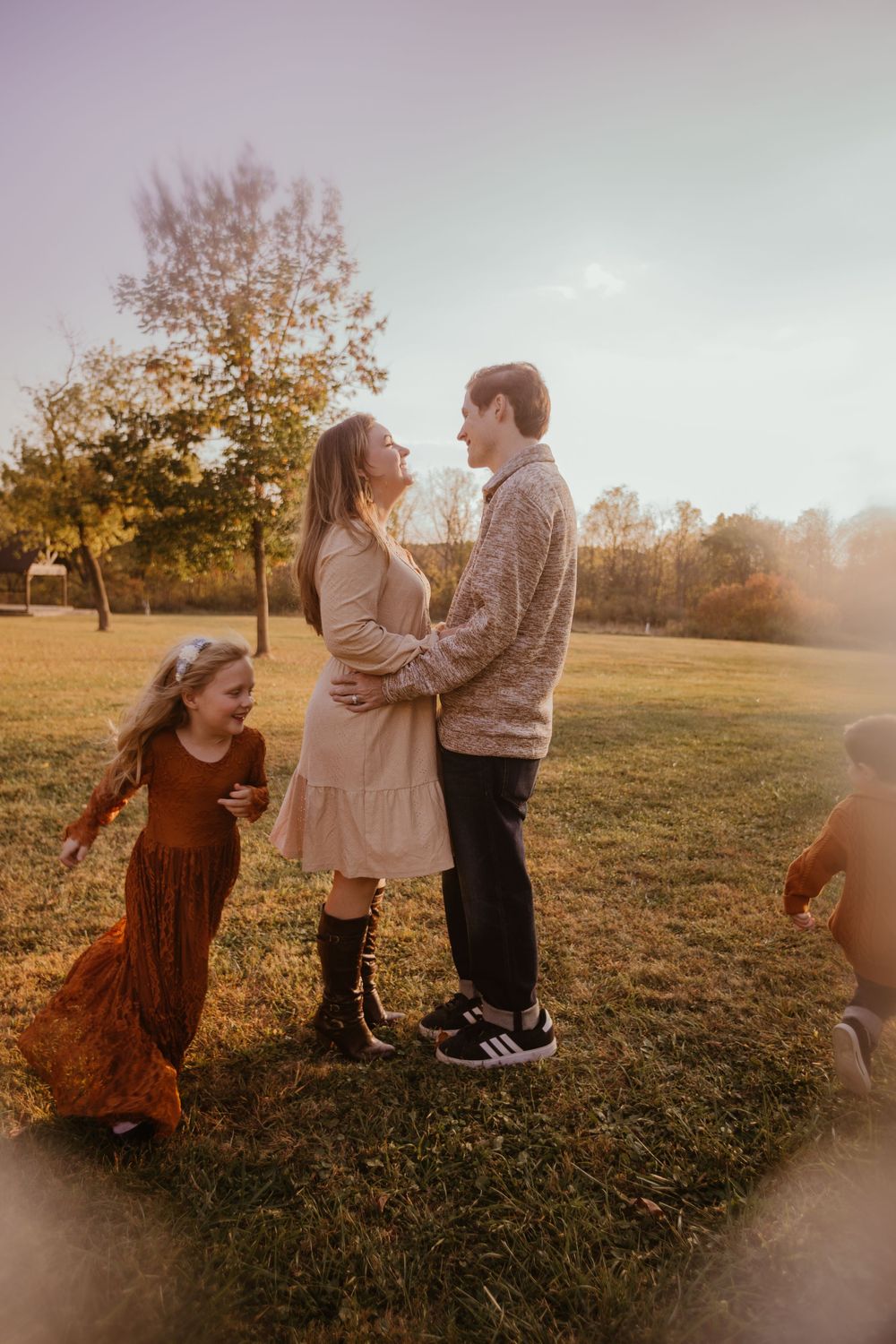 A tender moment unfolds between people in autumn attire on grass during golden hour.