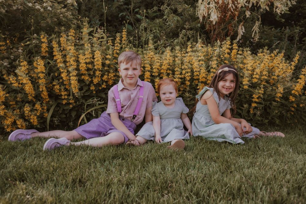 Seven connected outdoor family photos show people sitting together in a grassy field with golden flowers in background at sunset.