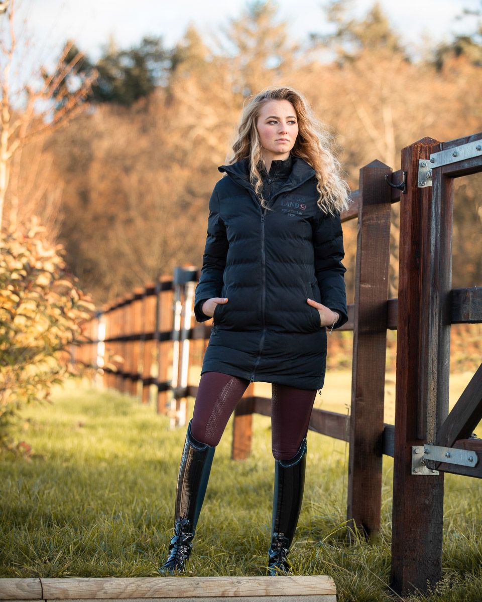 Winter fashion portrait outdoors featuring black puffer coat, mini skirt and tall boots against rustic wooden fence in nature.