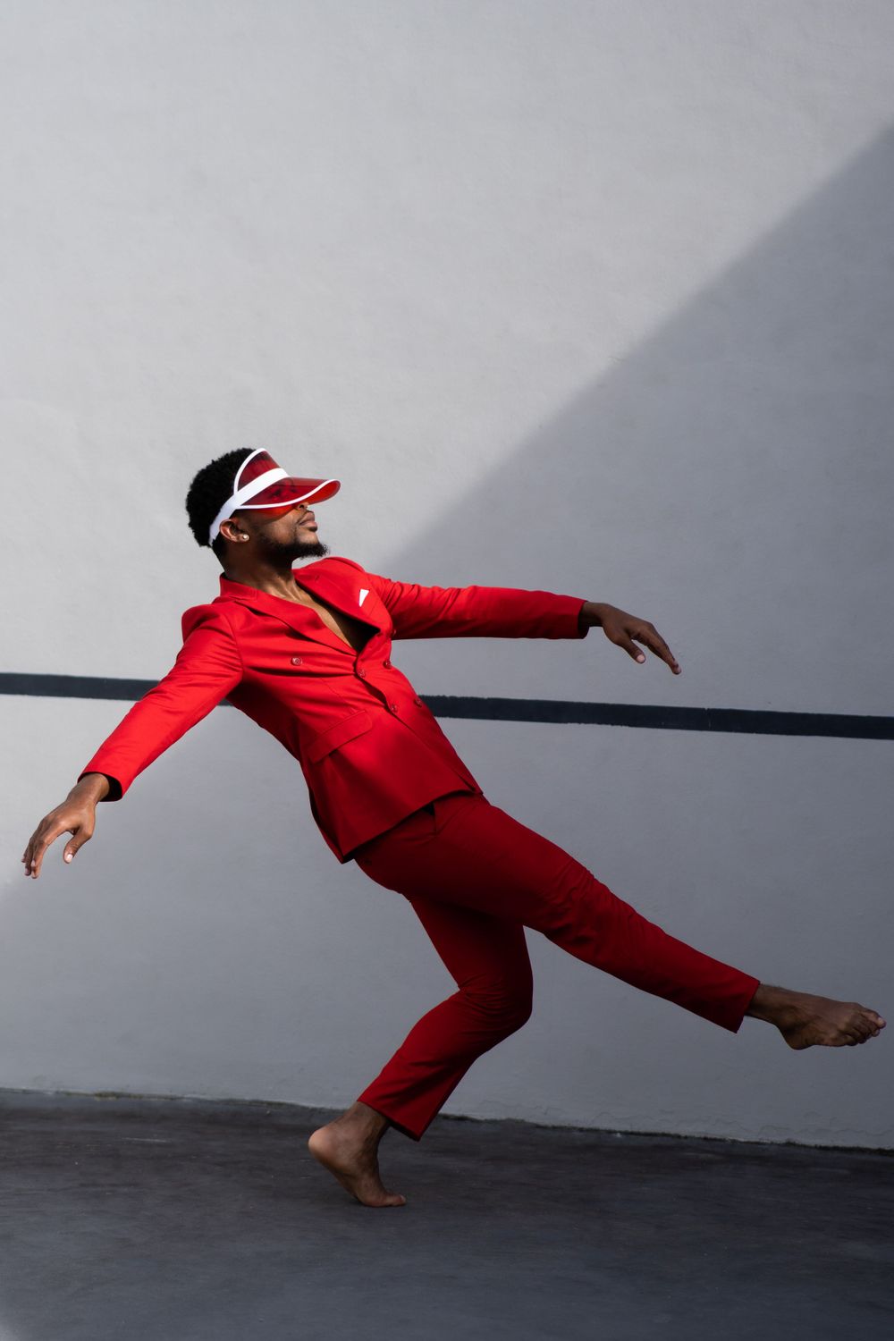 Dynamic pose in bright red suit and visor against minimalist grey wall background.