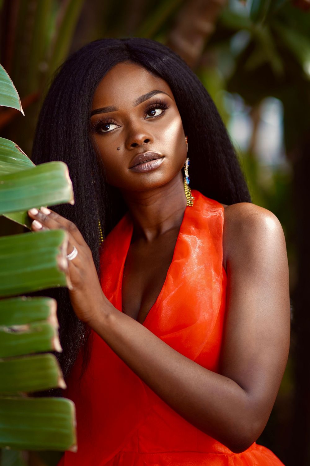Tropical portrait with red sleeveless top and palm leaves creating natural framing.