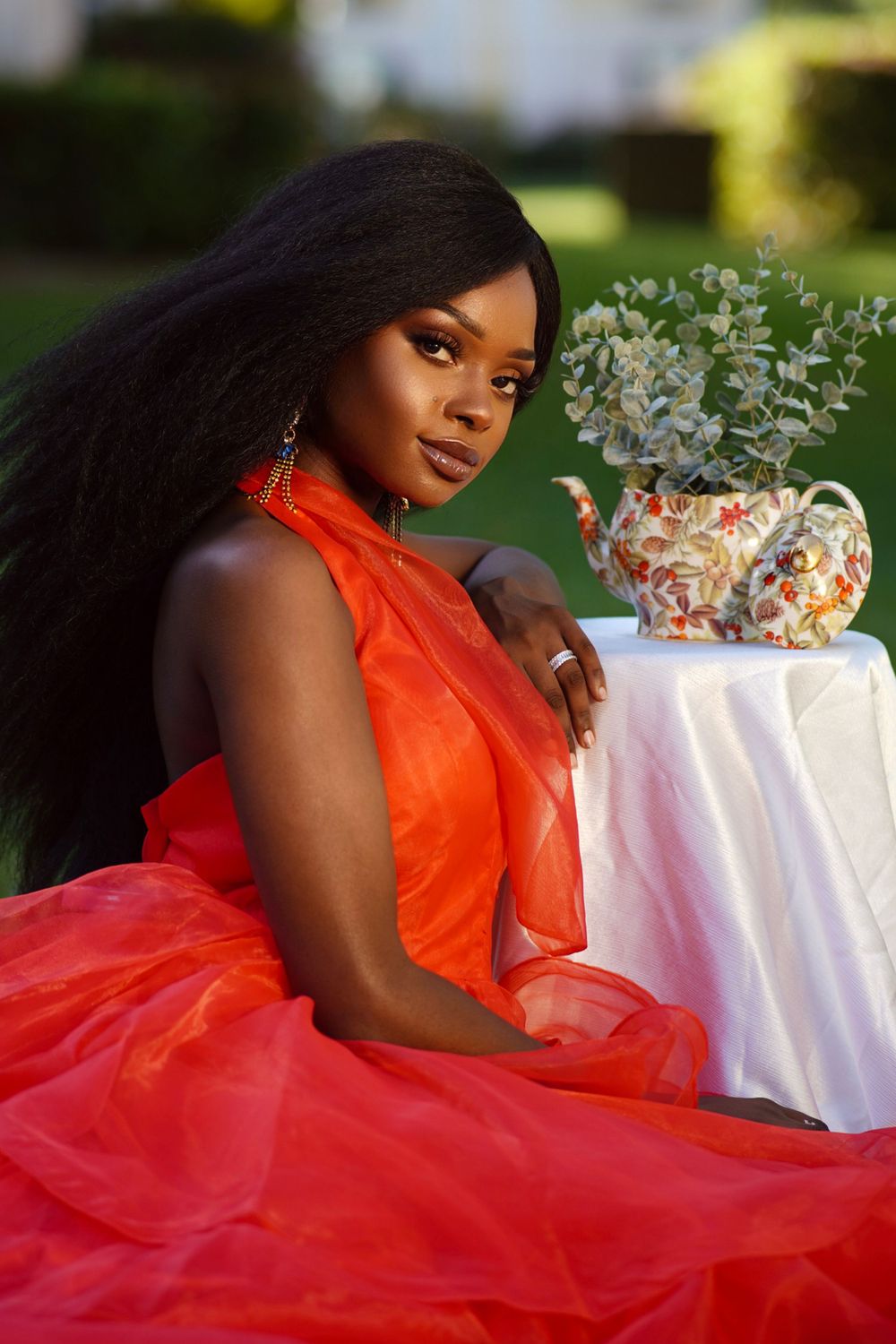 Elegant garden photoshoot featuring flowing red gown and floral centerpiece on white tablecloth.