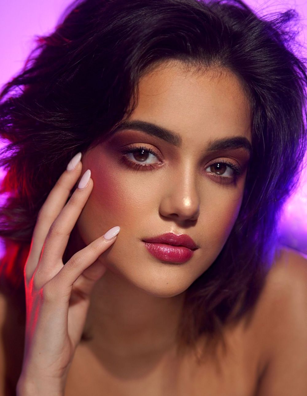 Beauty portrait with dramatic purple lighting showing glamorous makeup and manicured nails.