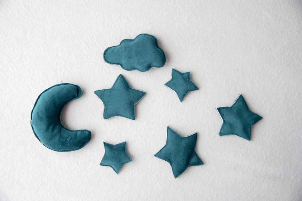 Set of teal blue fabric moon, stars and cloud shaped nursery cushions on white background.