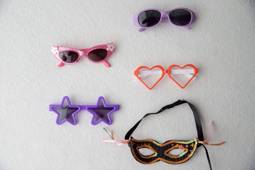 Collection of colorful novelty sunglasses and masquerade mask on white background.