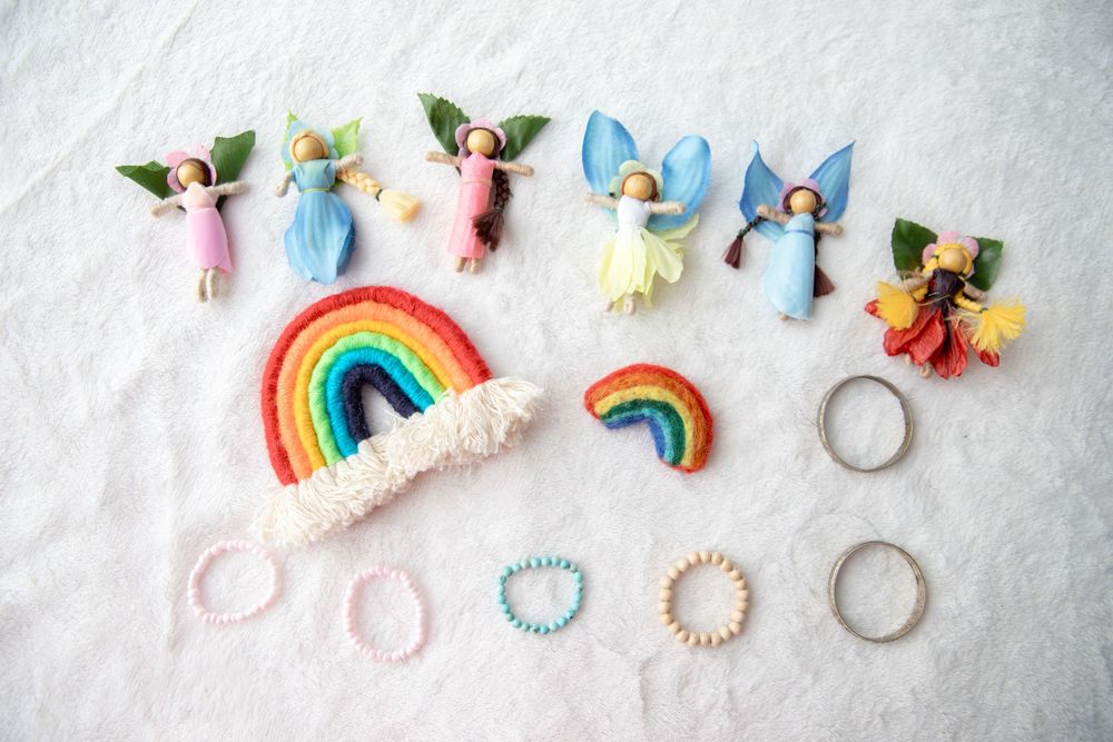 Colorful handmade fairy dolls with wings arranged around a felt rainbow on white background.