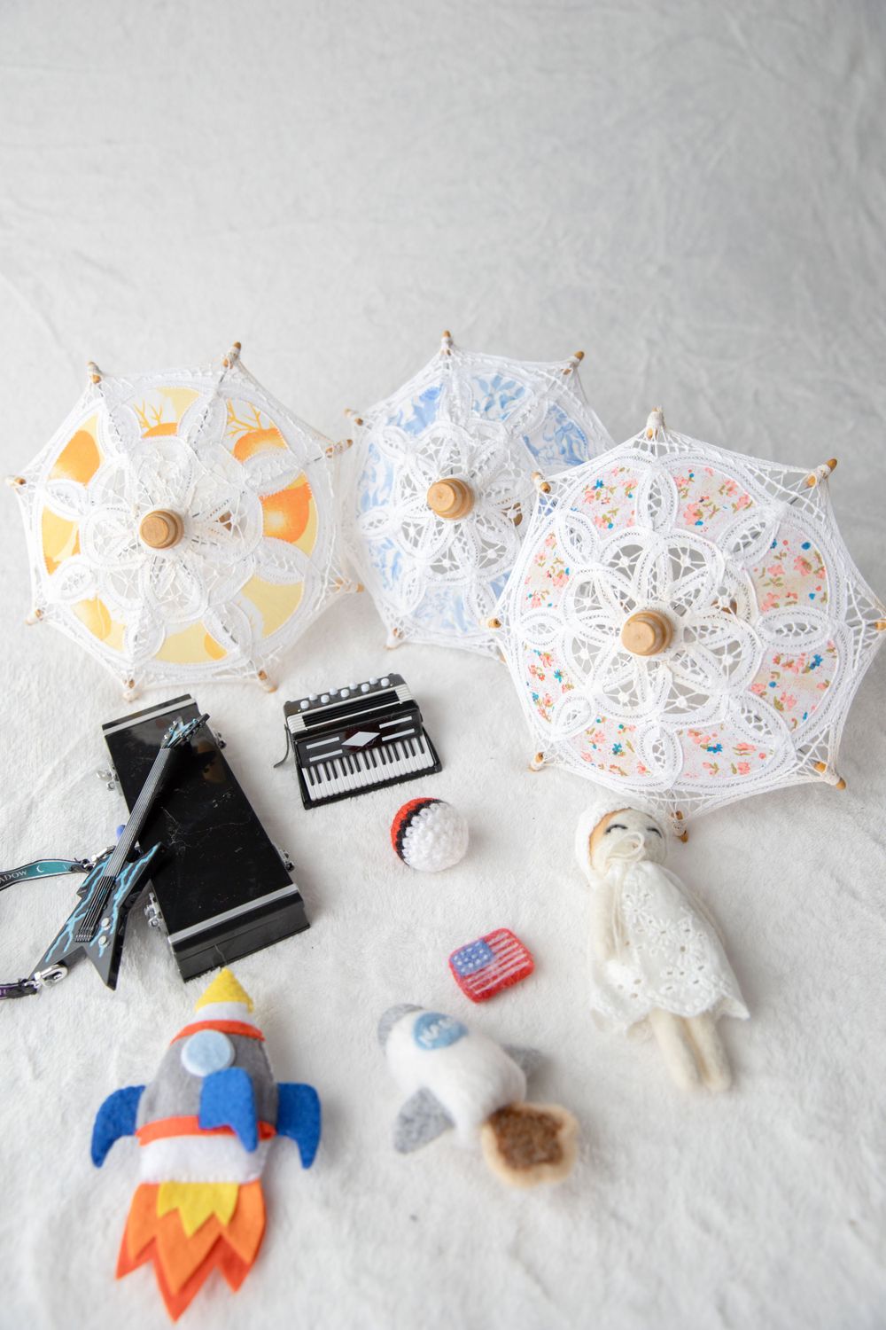 Flat lay of miniature props including lace parasols, rocket, doll, and small accessories.