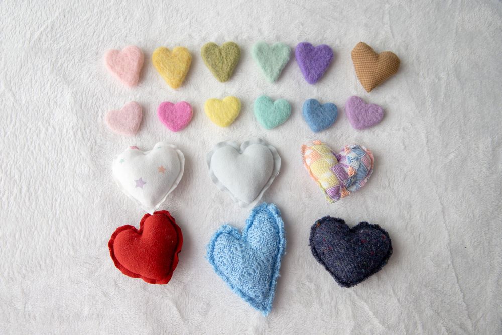 Collection of handmade fabric hearts in assorted colors and textures arranged on white background.