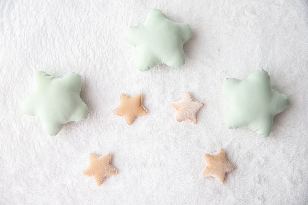 Soft mint green and peach star-shaped stuffed cushions arranged on white fluffy background.