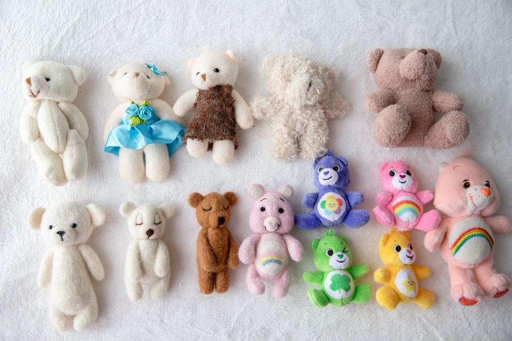 Assortment of small teddy bears and colorful Care Bears plush toys on white background.