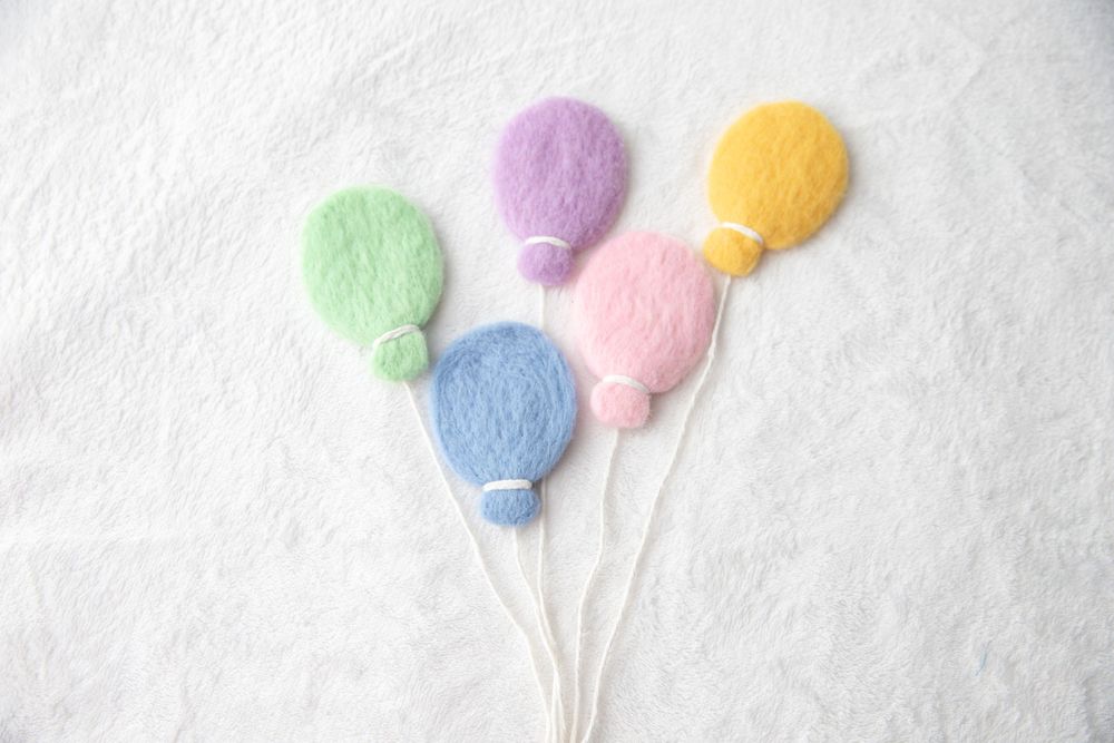 Five pastel felt wool balloons in green, blue, pink, purple, and yellow on a white background.