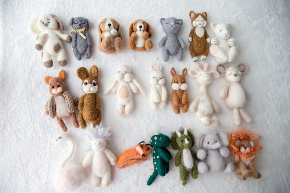 Collection of handmade felt and knitted miniature animal toys arranged on a white surface.