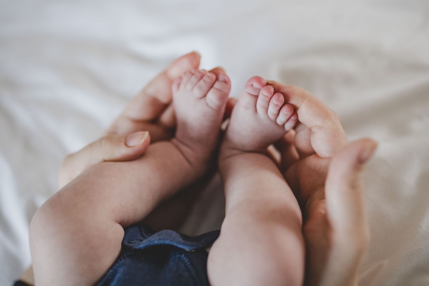 Close-up of tiny baby feet being held by gentle hands on white bedding.